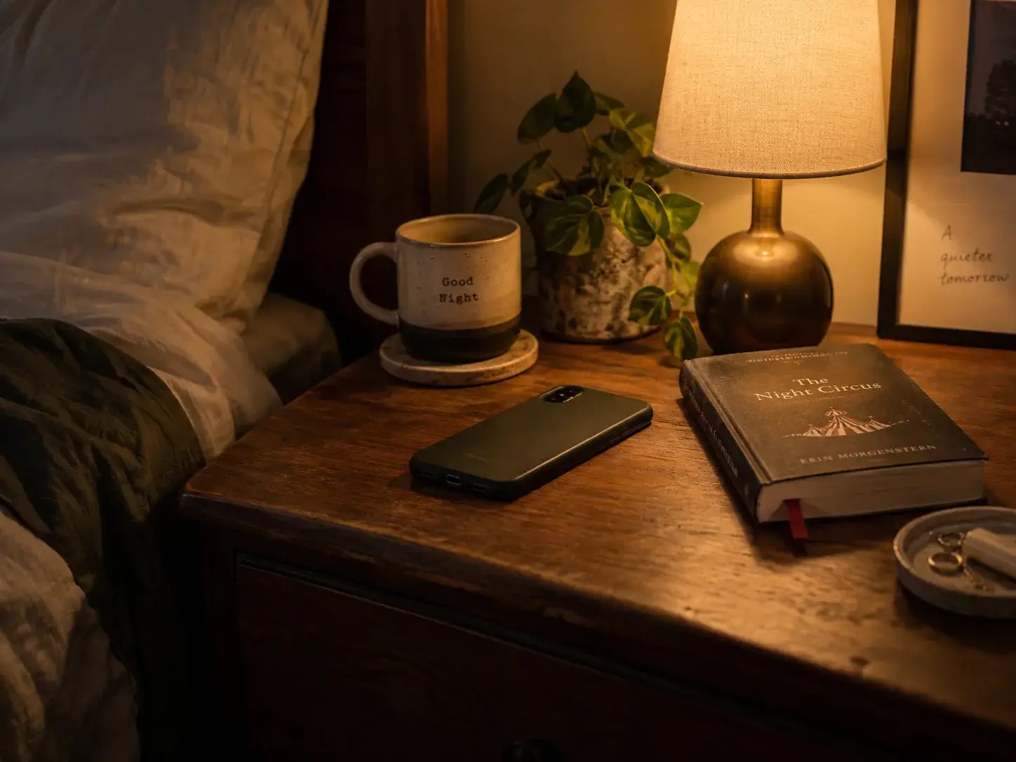 A nightstand at the end of the day with a phone face-down and a dim lamp